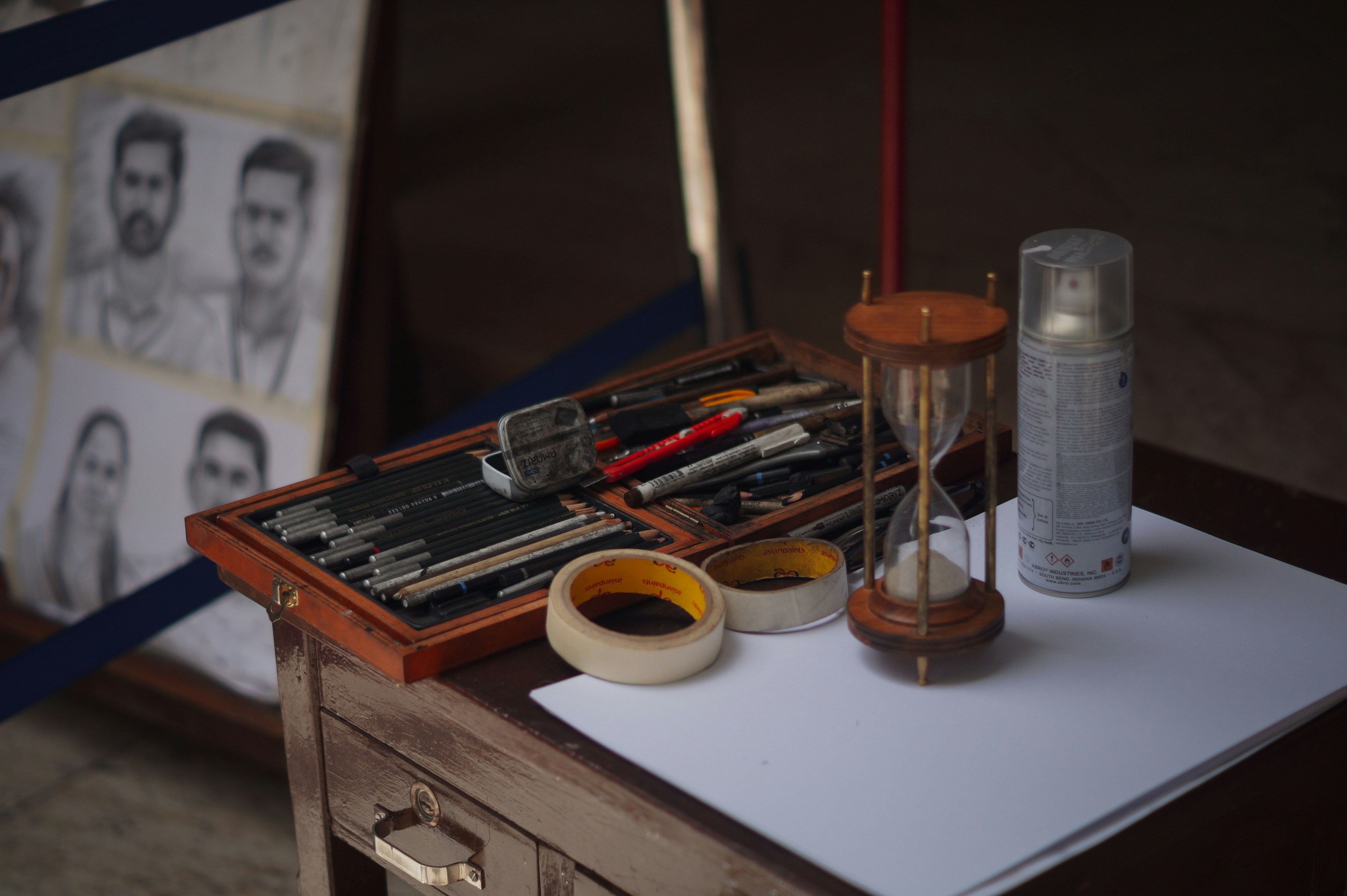 An artist's charcoal and drawing supplies laid out, with completed charcoal portraits pinned in the background