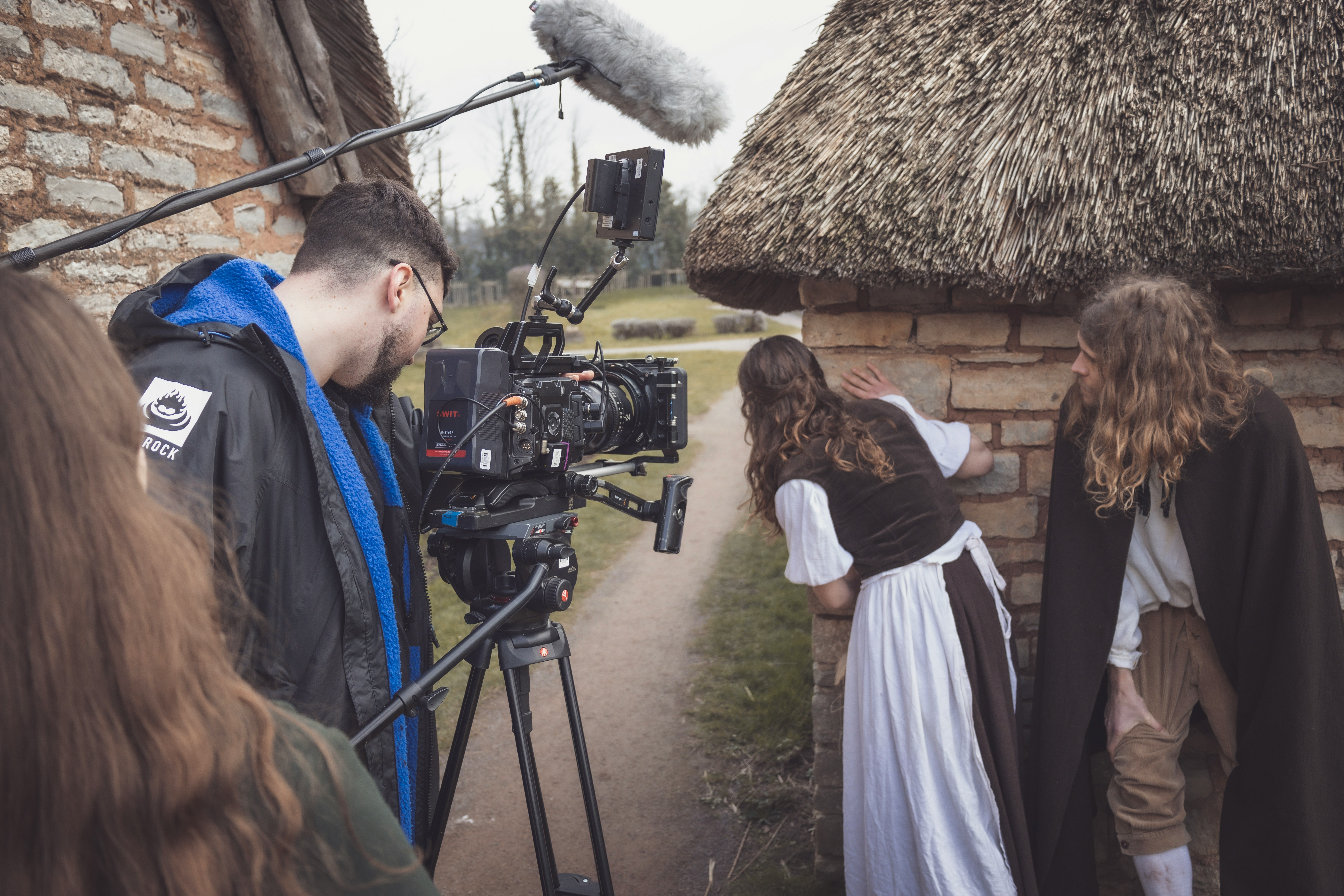 A film crew shooting a period drama outside a thatched stone cottage, with actors in period costume