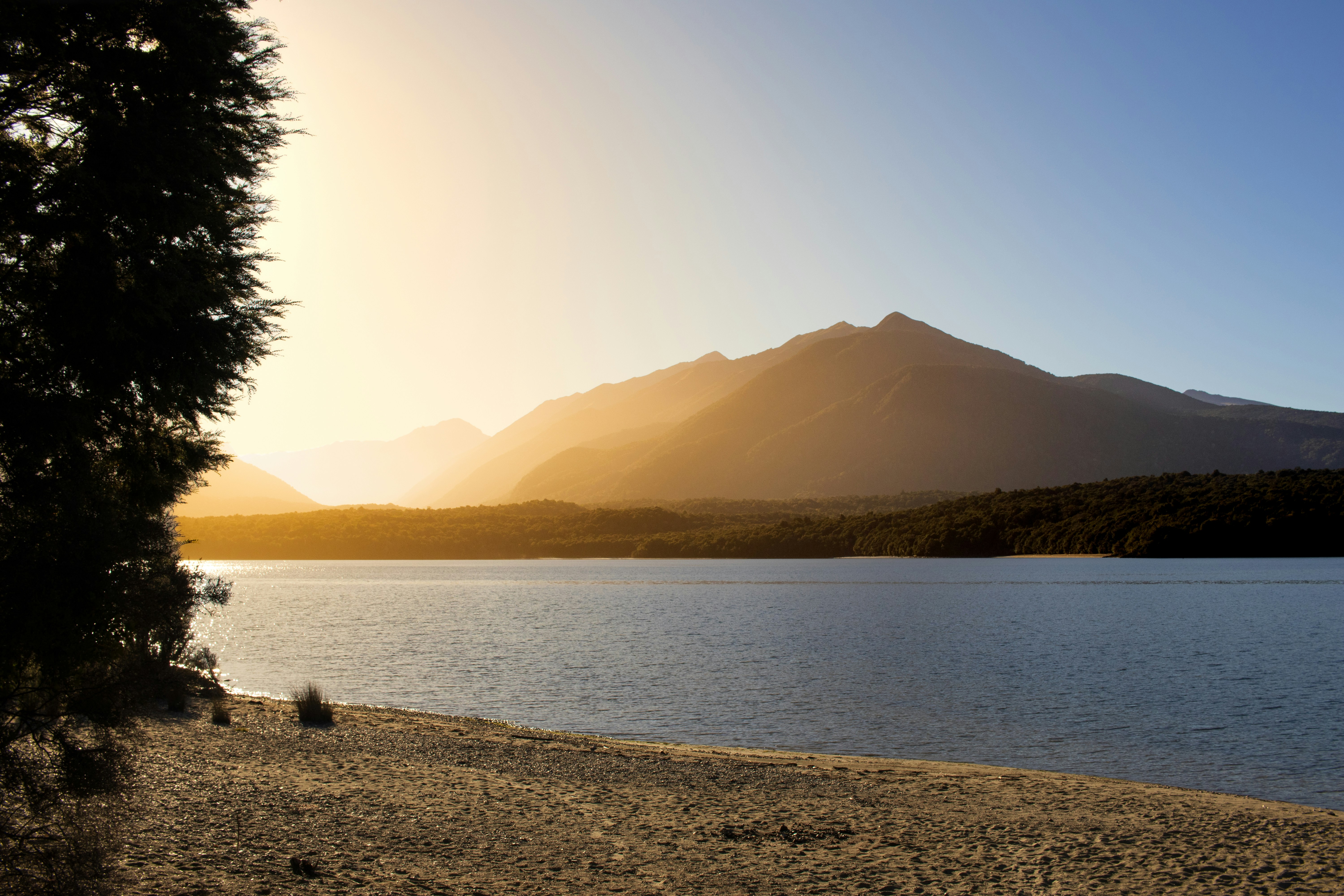 Golden sunset over a still mountain lake, low light catching the far peaks