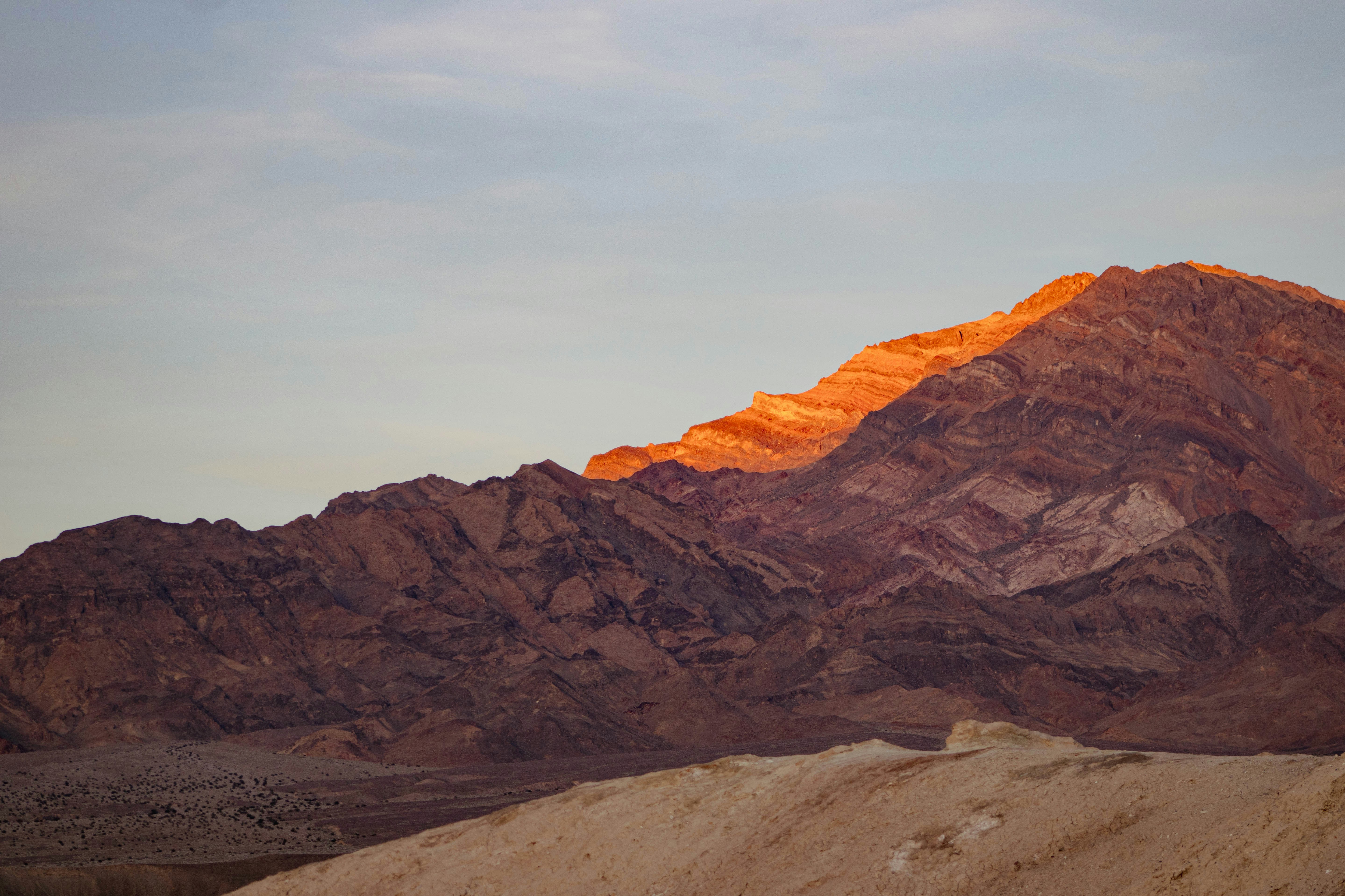 A desert mountain lit by dramatic orange sunset light striking the bare rock