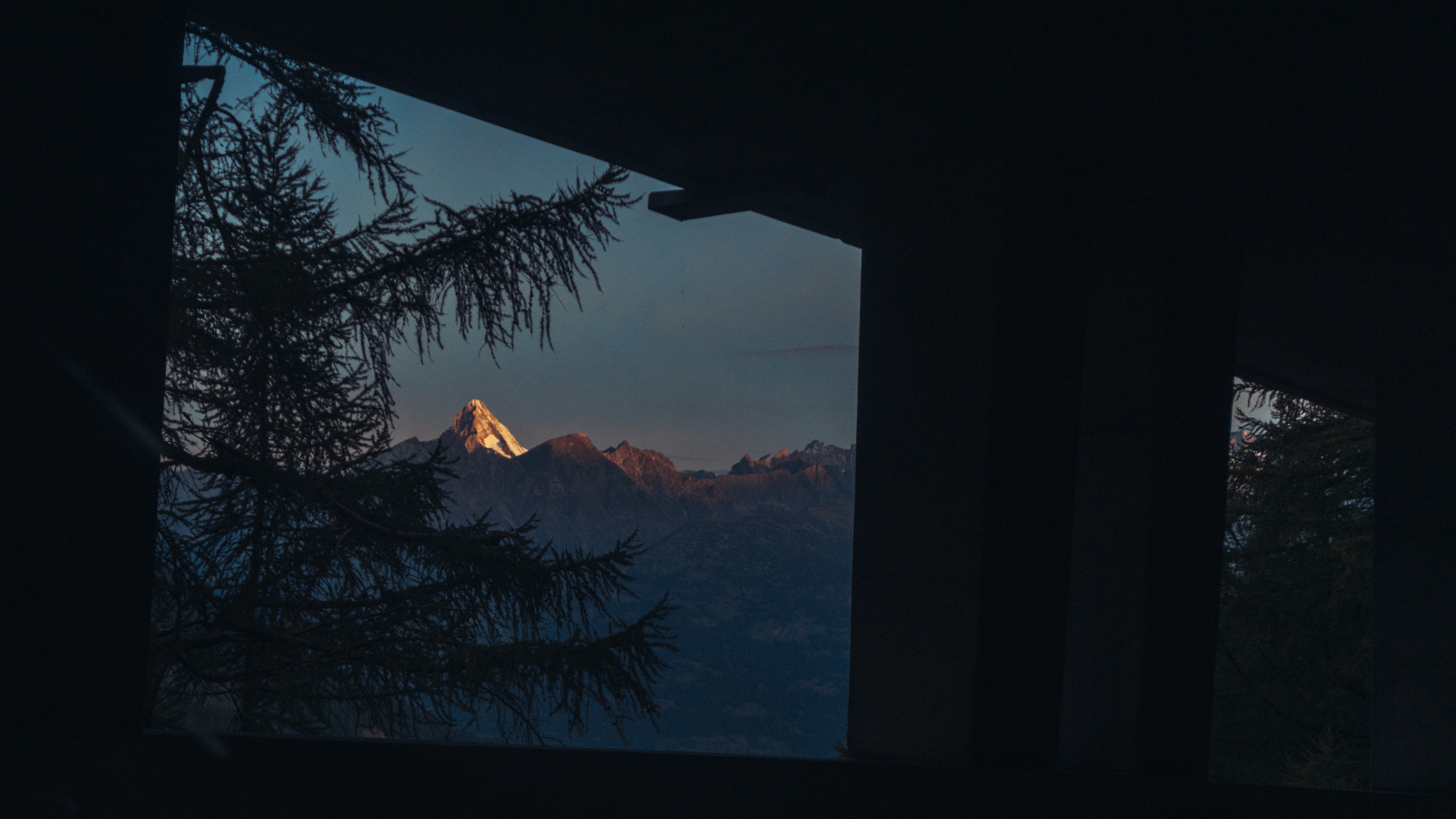 Alpine peaks catching the last dusk light, seen through a dark framed opening